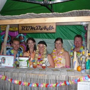 Guests in pirate-themed costumes behind a tiki bar labeled "RUMBar" at a Caribbean murder mystery party.